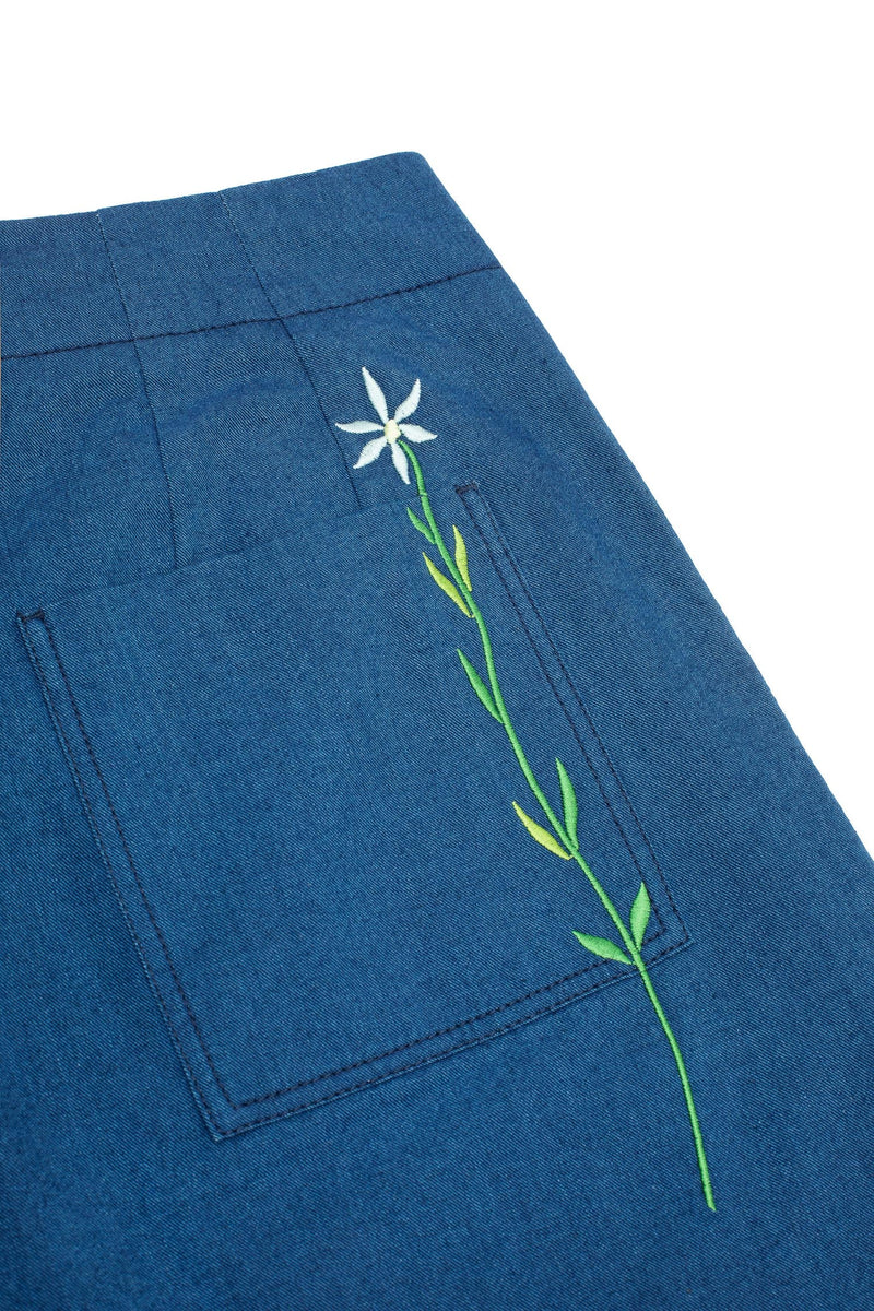 Product detail shot of Saywood's Amelia wide leg trousers in natural indigo Japanese denim, back close up of patch pocket and blue embroidered flower