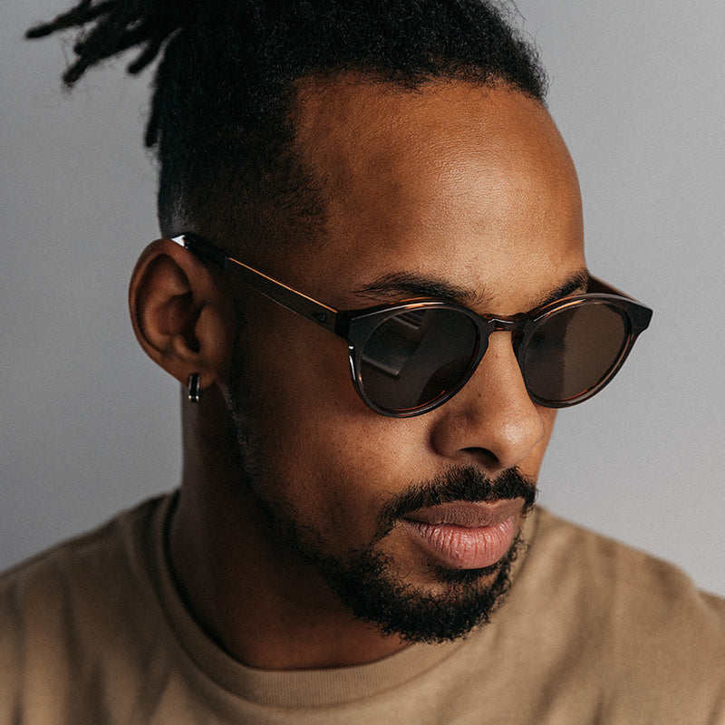 Black man wearing transparent brown acetate sunglasses with amber lenses looking down