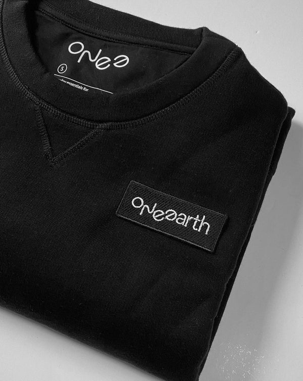 ONE Earth logo embroidered patch sewn onto black organic cotton sweatshirt on left hand side of chest. Shown folded.